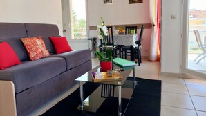 A living room with a grey sofa, red cushions, a small table with a plant, and a dining area with a table and chairs. - Apartment near sea and city (Antibes)