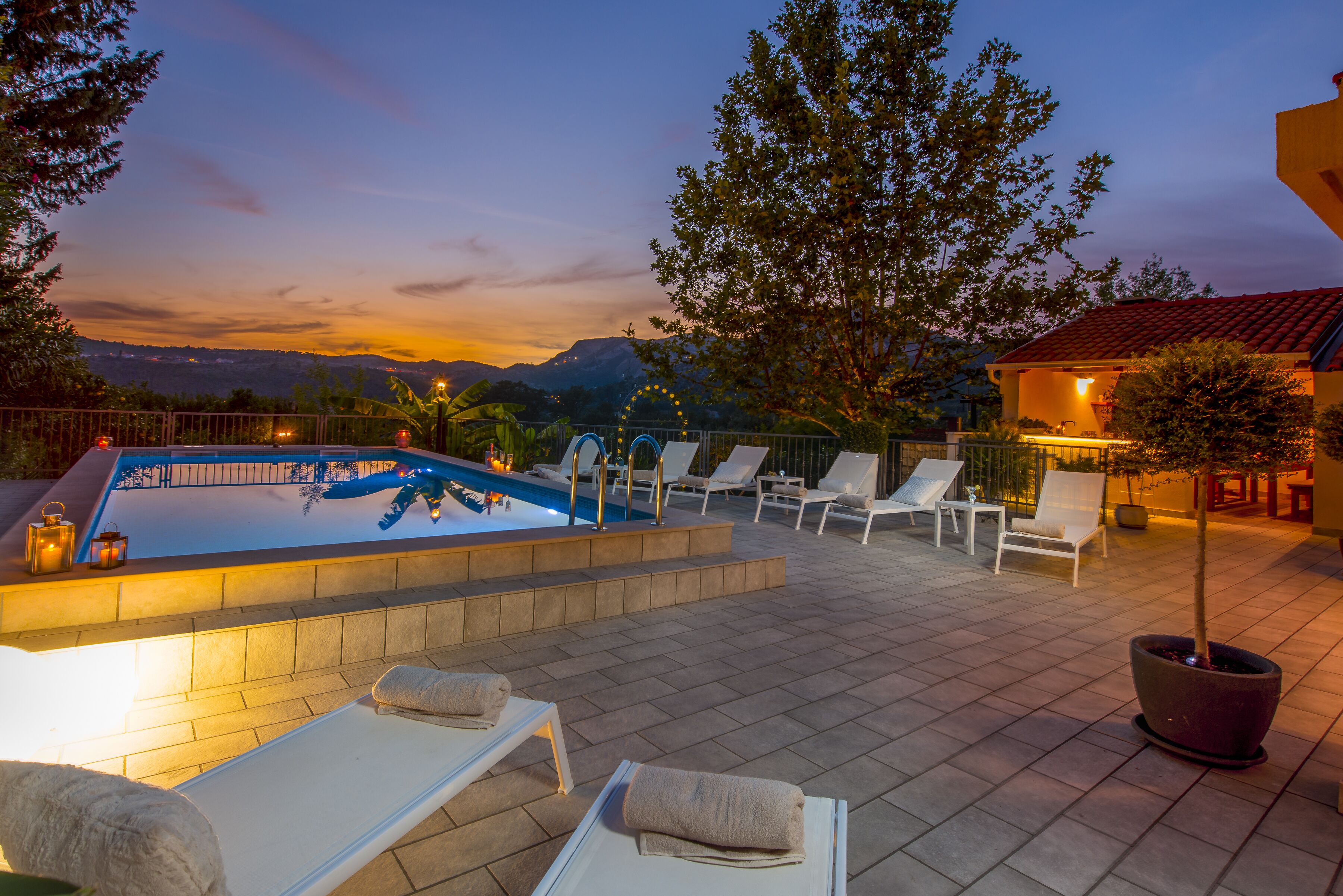 A pool area with lounge chairs and a view of the mountains at dusk.