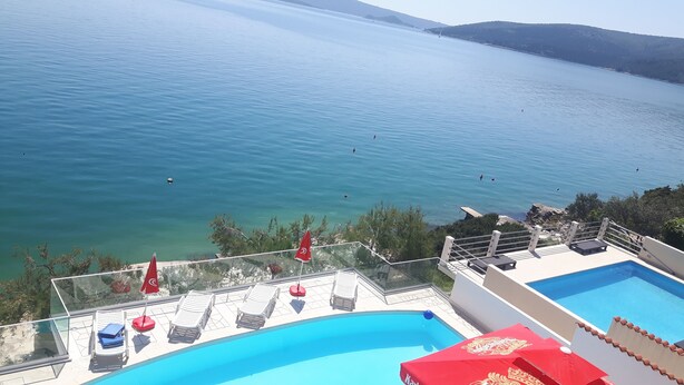 Ein Poolbereich mit klarem, blauem Wasser, Liegestühlen und Blick aufs Meer.