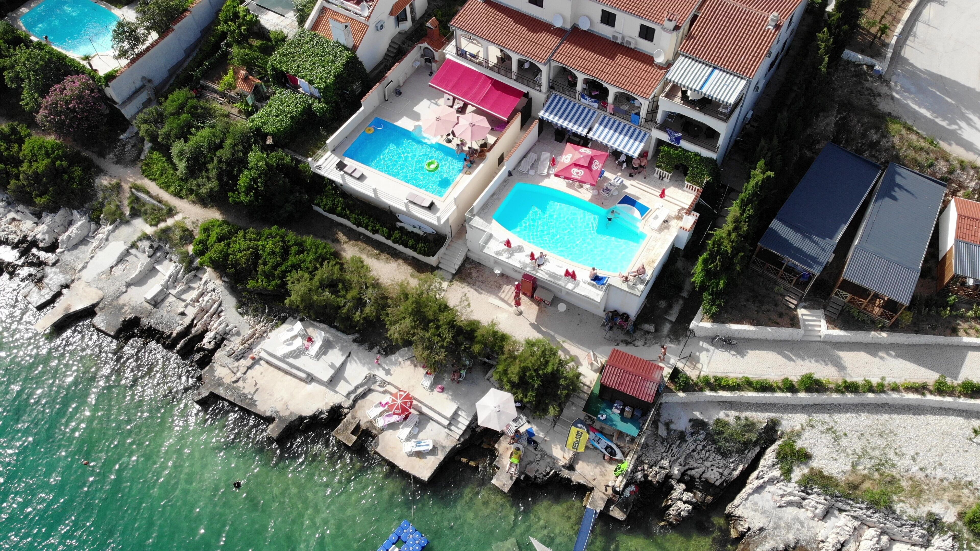 A coastal hotel with two swimming pools, a rocky shoreline, and a paved walkway.