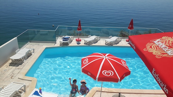 Una piscina con sillas de descanso y sombrillas, con vista a un cuerpo de agua.