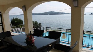 Eine Terrasse mit Pool, Esstisch und Stühlen mit Blick auf ein Gewässer und Segelboote.
