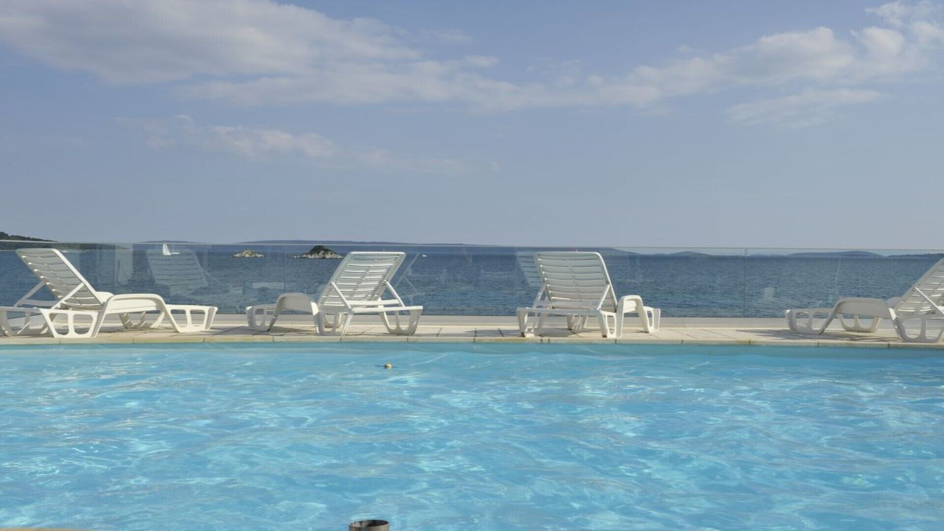 Uma área à beira da piscina com espreguiçadeiras e vista para o mar.