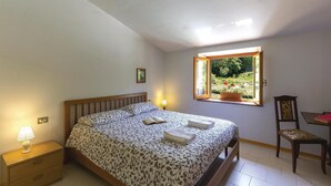 A bedroom with a bed, bedside table, lamp, window, chair, and a small table with books. - Gorgeous home in Sassalbo -MS- (Sassalbo -MS-)