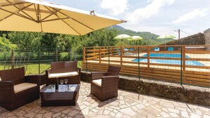 A patio with wicker furniture and a glass table, overlooking a pool area with a wooden fence and umbrellas. - Gorgeous home in Sassalbo -MS- (Sassalbo -MS-)
