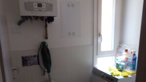 A compact laundry room with a washing machine, a mop, and a red storage unit.