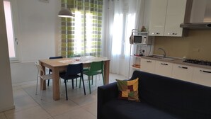 A modern kitchen with white cabinets, a dining table with chairs, and a sofa.