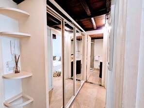 Stylish hallway with a mirrored wall reflecting a cozy bedroom with a bed and nightstand.