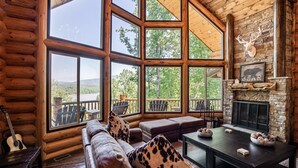 A log cabin interior with large windows, a fireplace, a sofa, and a dining table.