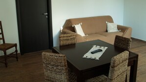 A living room with a brown sofa, two wicker chairs, a wooden table, and a black door.