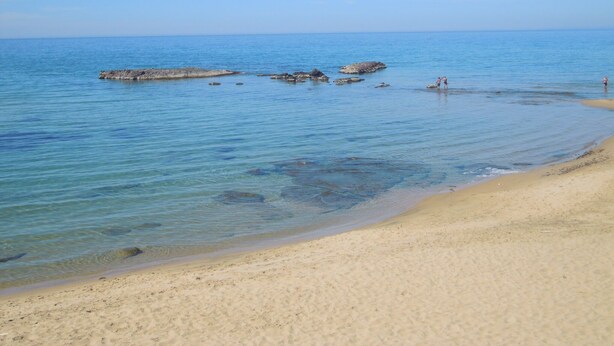 A beach with clear water, sandy shore, and rocky outcrops.
