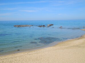 A beach with clear water, sandy shore, and rocky outcrops.