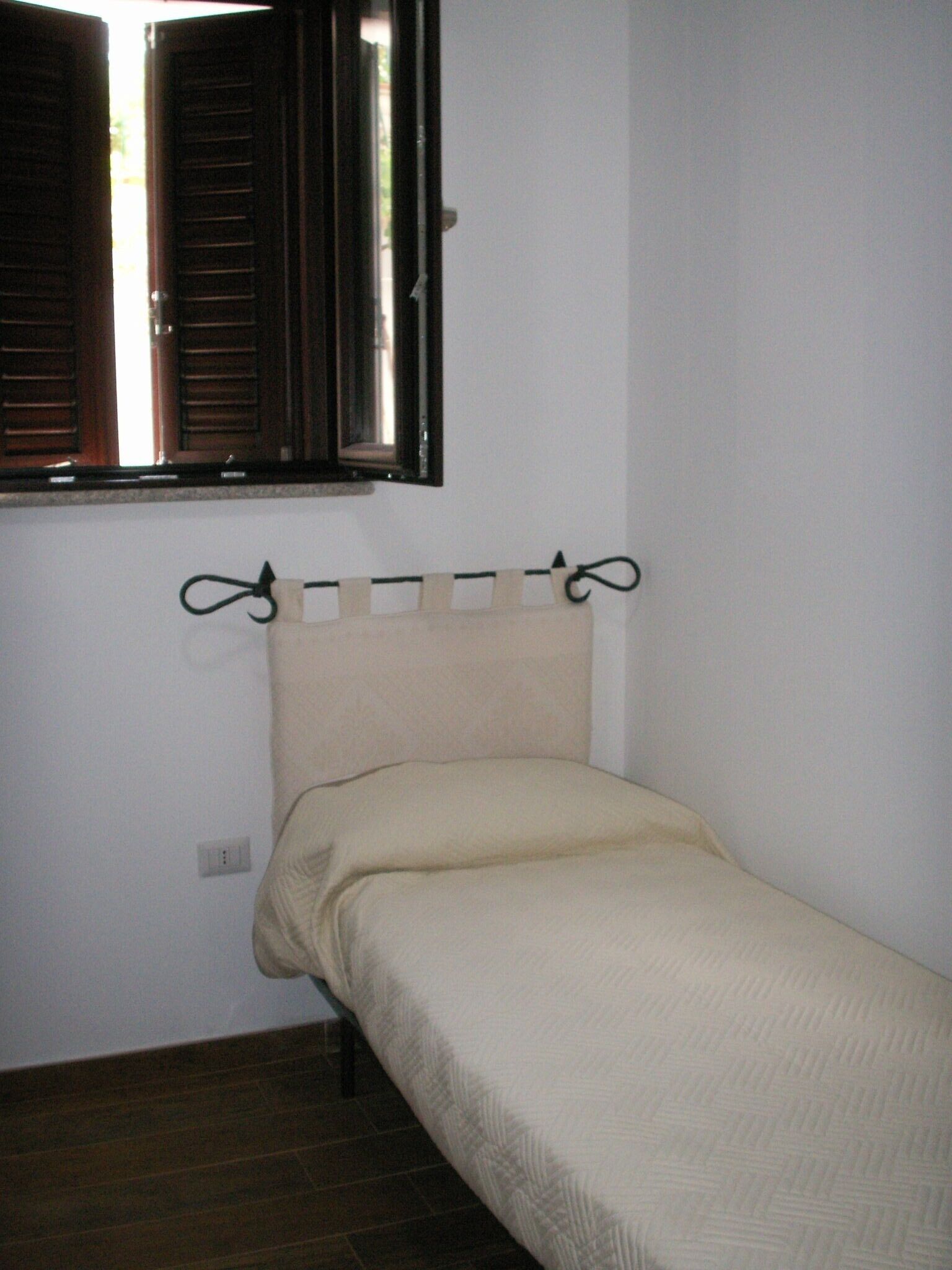 A small, single-bed room with a wooden headboard and a window with open shutters.