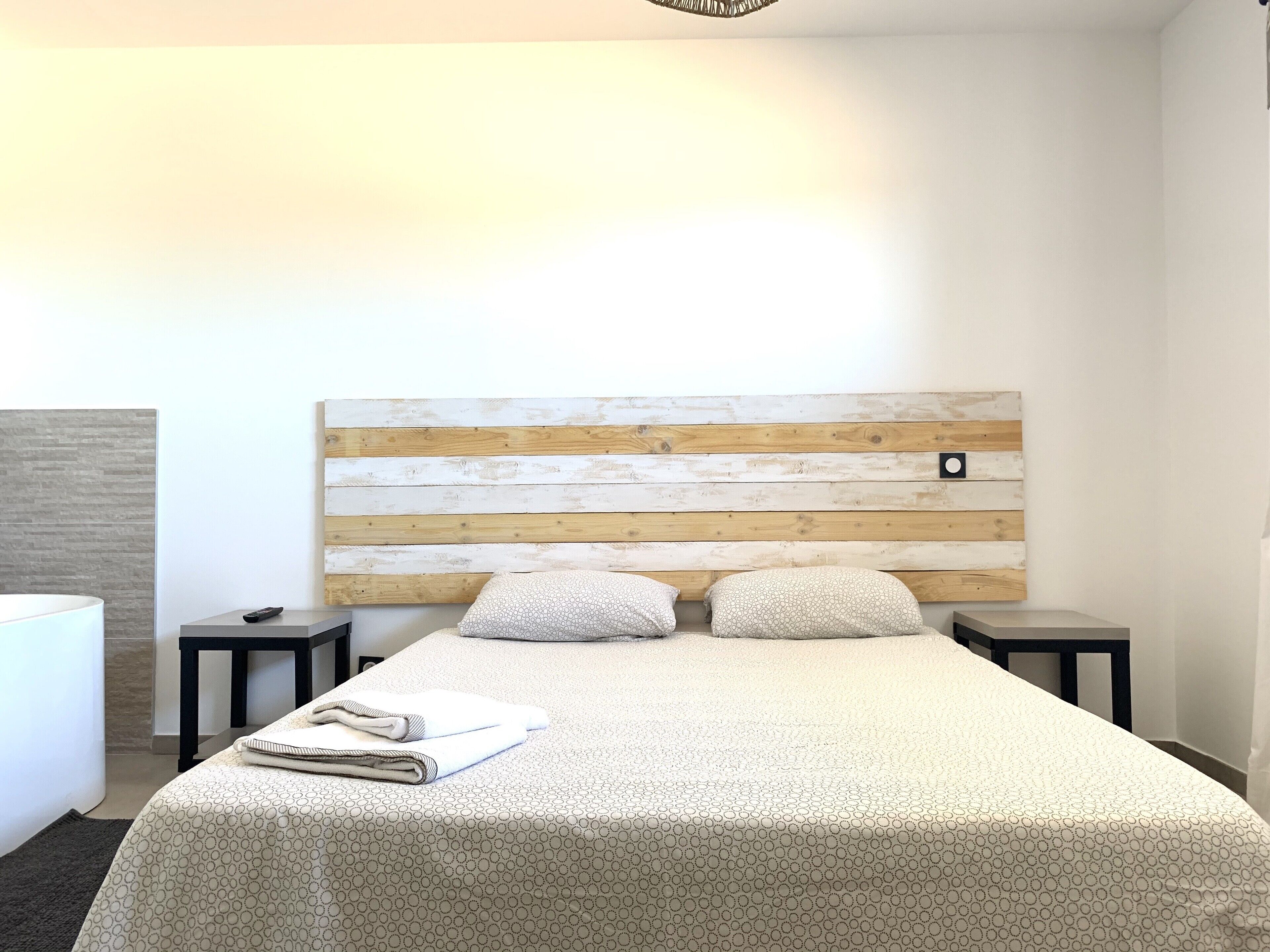A hotel room with a wooden headboard, two bedside tables, a bed with a patterned bedspread, and a folded towel on the bed.