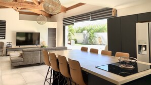 A modern kitchen with a large island, a dining area, and a living space with a sofa and TV. - Pool Villa Near Beach (Agde)
