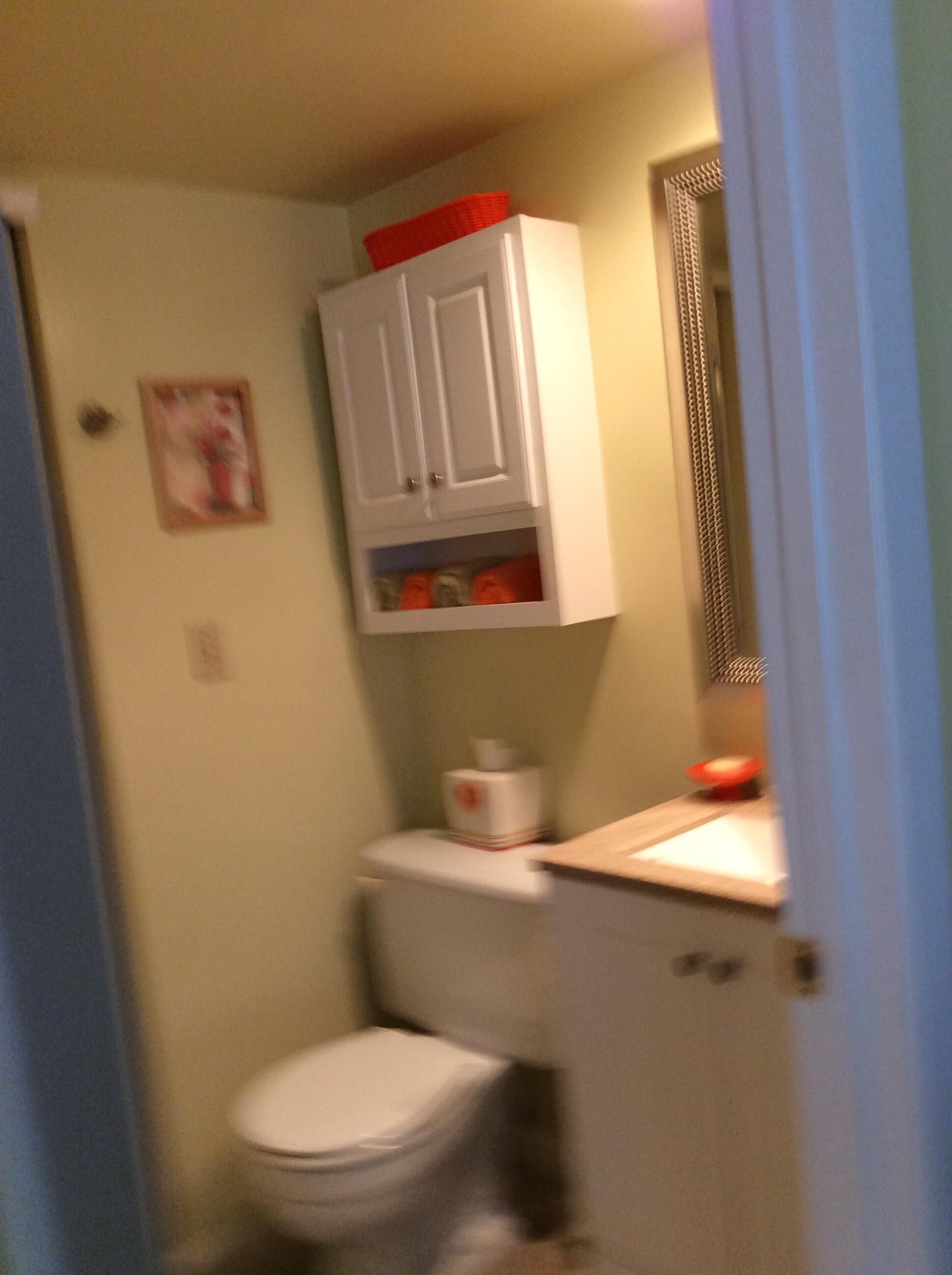 Un baño pequeño con inodoro, un armario sobre el inodoro y un espejo en la pared.