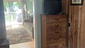 A bedroom with a bed, a wooden dresser, a television, and a door leading to a balcony. - Lakefront Cozy Cottage  (Rockport)