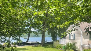 A well-maintained lawn with a wooden deck and a house with a white exterior. - Lakefront Cozy Cottage  (Rockport)