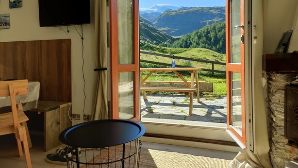 Une chambre avec un lit en bois, une petite table, un téléviseur et une grande fenêtre donnant sur un paysage montagneux.