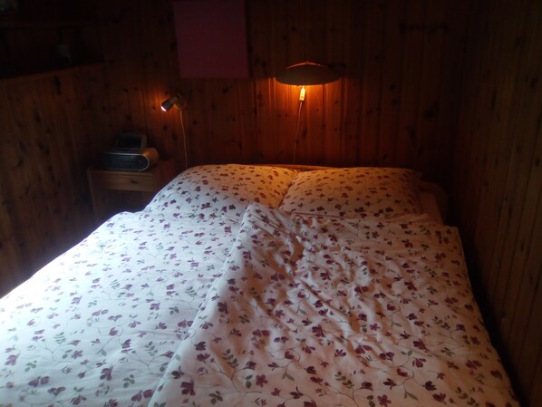 Una stanza in legno con un letto rivestito da biancheria da letto floreale.