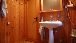 Ein Badezimmer mit Holzwandverkleidung, einem weißen Waschbecken, einem Handtuch an der Wand und einem Spiegel über dem Waschbecken.