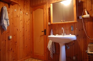 Un bagno con rivestimenti in legno, un lavandino bianco, un asciugamano appeso al muro e uno specchio sopra il lavandino.