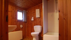 Ein Badezimmer mit Holzwandverkleidung, einer Toilette, einem Waschbecken und einer Badewanne.