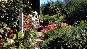 Ein Garten mit verschiedenen Pflanzen und Blumen, ein Holzzaun und ein Gebäude mit roter Fassade.