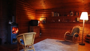 Ein gemütliches Blockhaus-Interieur mit Kamin, Korbsesseln, Fernseher und Lampe.