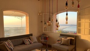 Un salón acogedor con sofá, sillón y mesa de centro, con un gran ventanal que ofrece vistas a un puente y un paisaje.