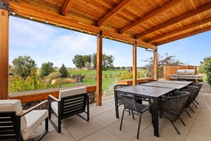 Eine Terrasse im Freien mit einer Holz-Pergola, einem Tisch, Stühlen und einem Grill im Hintergrund.