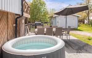 A hot tub on a wooden deck, outdoor furniture, a barbecue grill, and a shed.