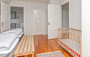 A bedroom with a bed, a wooden bench, a crib, and a bathroom visible through an open door. - Stunning home in Hultsfred with sauna (Hultsfred)