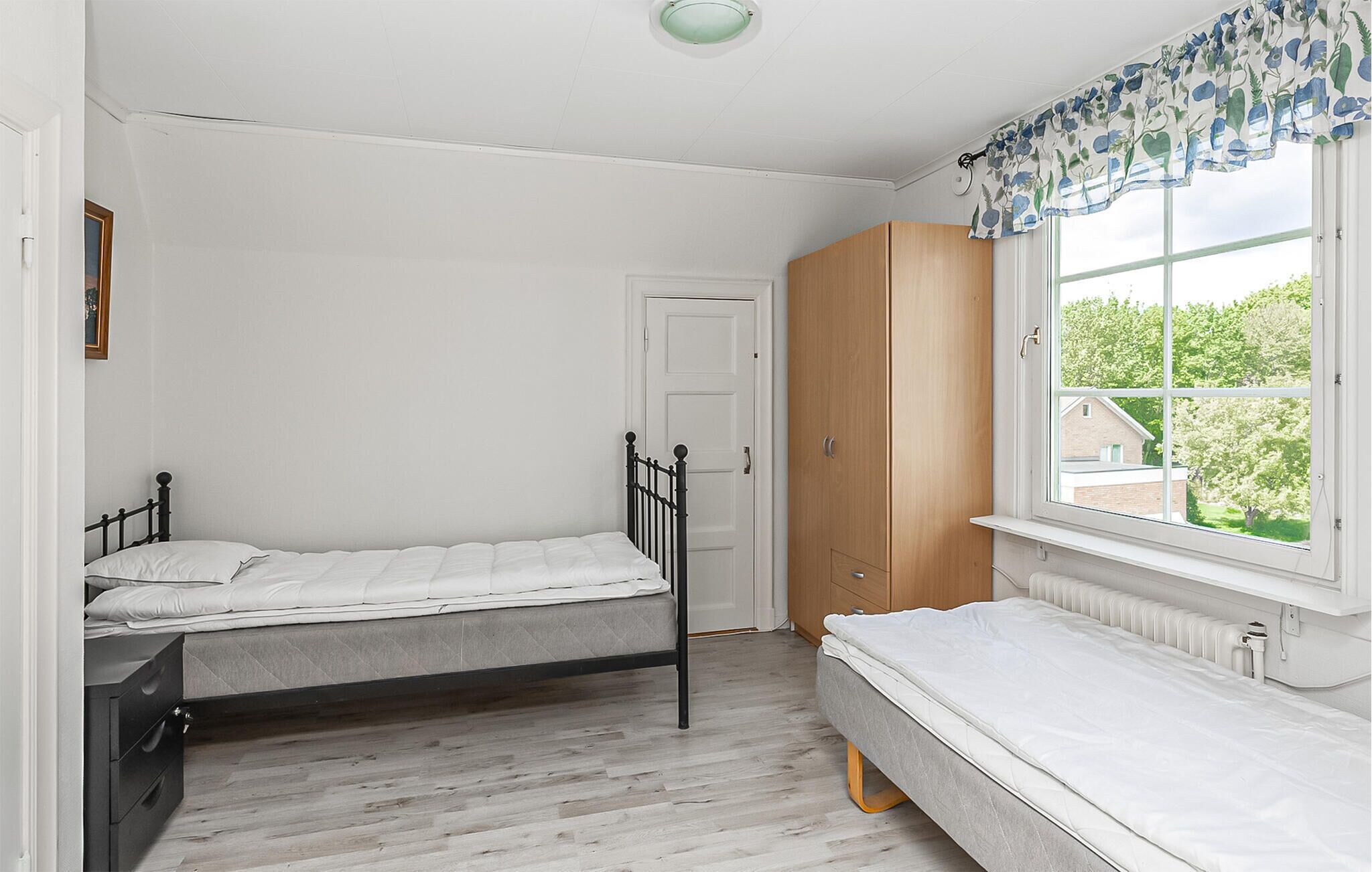 Ein Schlafzimmer mit zwei Einzelbetten, einem Holzschrank, einem Fenster mit Blick auf Grünflächen und einer weißen Tür.