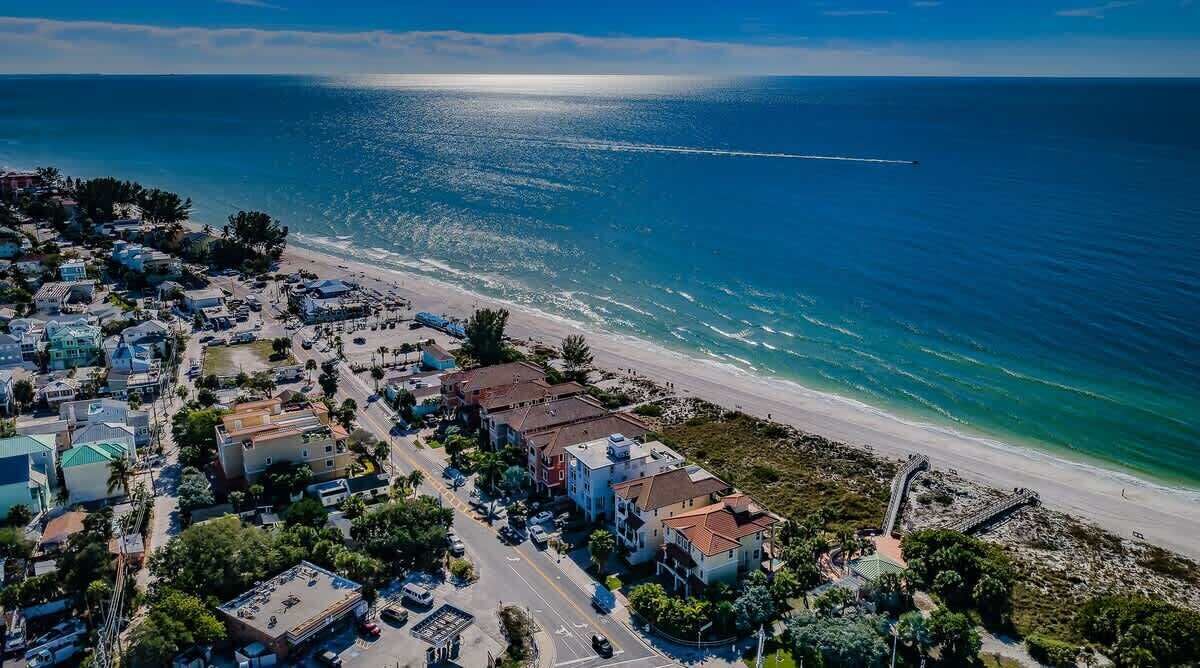 Vista aerea di una località costiera con spiaggia, edifici e cielo sereno.