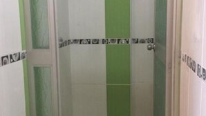 Een kleine badkamer met groene en witte tegels, een toilet en een douchecabine.
