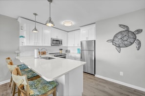 A modern kitchen with white cabinets, stainless steel appliances, a central island with seating, pendant lighting, and a wall mural of a turtle.