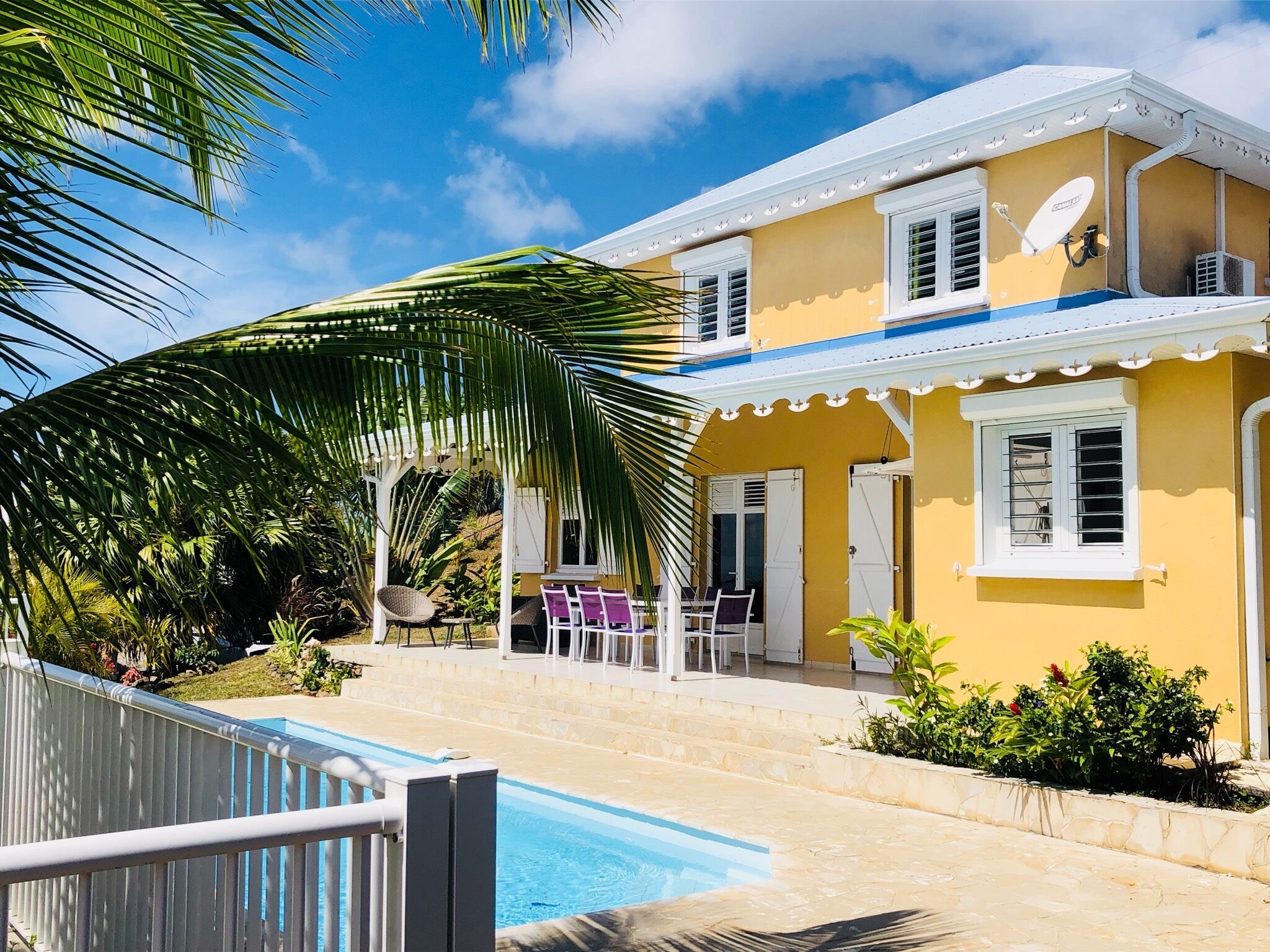 Un edificio amarillo con piscina, palmeras y un patio cubierto.