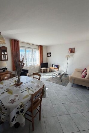 Een woonkamer met een eettafel, bank, televisie en een lamp.