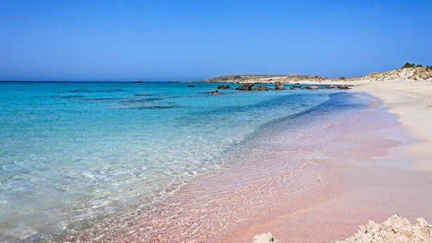 Une plage à l’eau turquoise et limpide, avec un rivage sablonneux et des affleurements rocheux.
