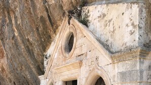 Un petit bâtiment en pierre, doté de fenêtres en arc et d’un dôme central, adossé à une falaise rocheuse.