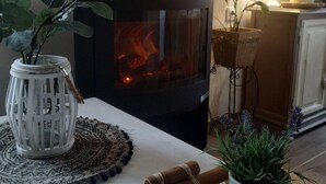 A cozy room with a wood-burning stove, a white vase with green leaves, and a small table with a woven placemat. - RUSTIC VACATION HOUSE (Mondariz)