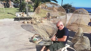 Un uomo seduto su una panchina in un parco con grandi strutture intrecciate e vista sul mare.