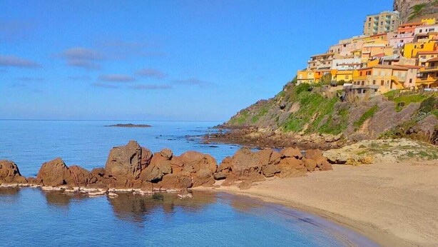Una zona costiera con acque blu cristalline, un litorale roccioso e edifici colorati su una collina.