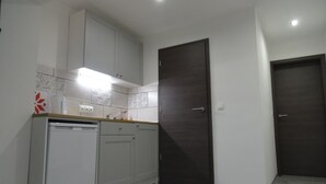Una cocina compacta con armarios blancos, lavavajillas integrado, una puerta de madera oscura y un salpicadero de azulejos.