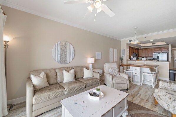 A living room with a beige sofa, a white coffee table, and a kitchen area in the background. - Seawind 1207 by Liquid Life (Gulf Shores)