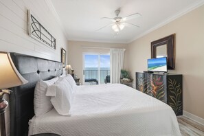 A hotel room with a large bed, a ceiling fan, a television, and a view of the outdoors. - Seawind 1207 by Liquid Life (Gulf Shores)
