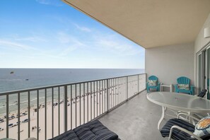 A balcony with a view of the beach, a table, chairs, and a sofa.