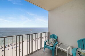 Ein Balkon mit Blick auf einen Strand, zwei türkisfarbene Stühle und ein kleiner weißer Tisch.