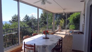 A sunlit balcony with a table and chairs, large windows offering a view of trees and hills. - houses / villas - 5 rooms - 6/8 persons (Magagnosc)